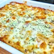 Homemade Italian Grinder Pasta Bake in a white casserole dish, topped with bubbly golden-brown melted cheese and sprinkled with Italian herbs.