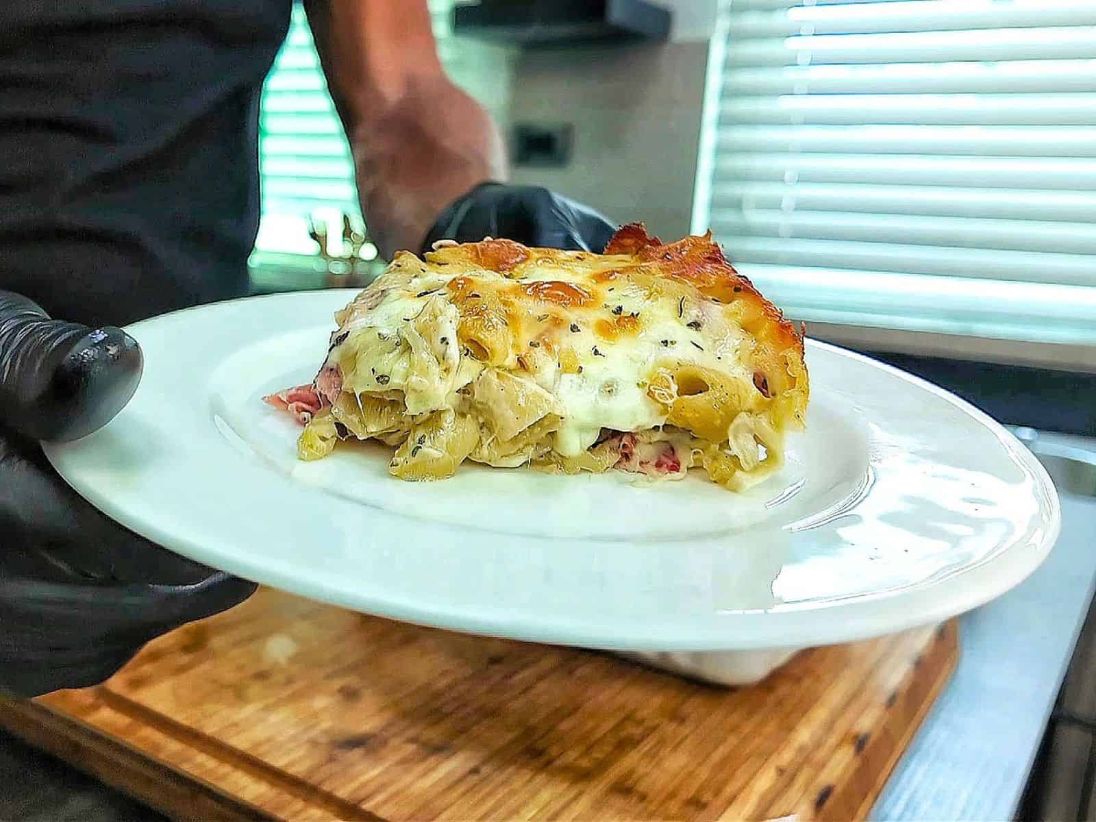 Homemade Italian Grinder Pasta Bake in a white casserole dish, topped with bubbly golden-brown melted cheese and sprinkled with Italian herbs.