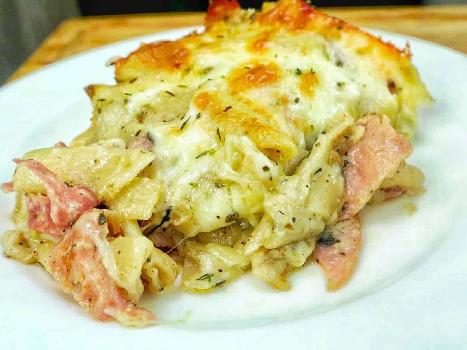 Homemade Italian Grinder Pasta Bake in a white casserole dish, topped with bubbly golden-brown melted cheese and sprinkled with Italian herbs.