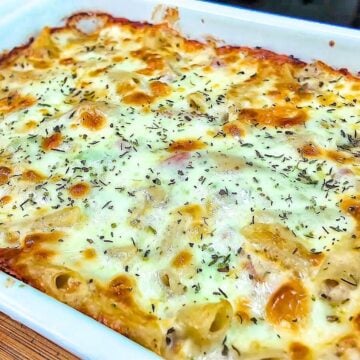 Homemade Italian Grinder Pasta Bake in a white casserole dish, topped with bubbly golden-brown melted cheese and sprinkled with Italian herbs.