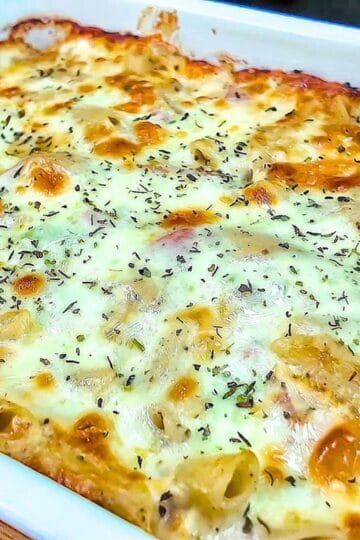Homemade Italian Grinder Pasta Bake in a white casserole dish, topped with bubbly golden-brown melted cheese and sprinkled with Italian herbs.