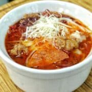Homemade Meat Lovers Pizza Soup in a white bowl, loaded with Italian sausage, pepperoni, bacon, rich tomato broth, and shredded mozzarella and Parmesan cheese.