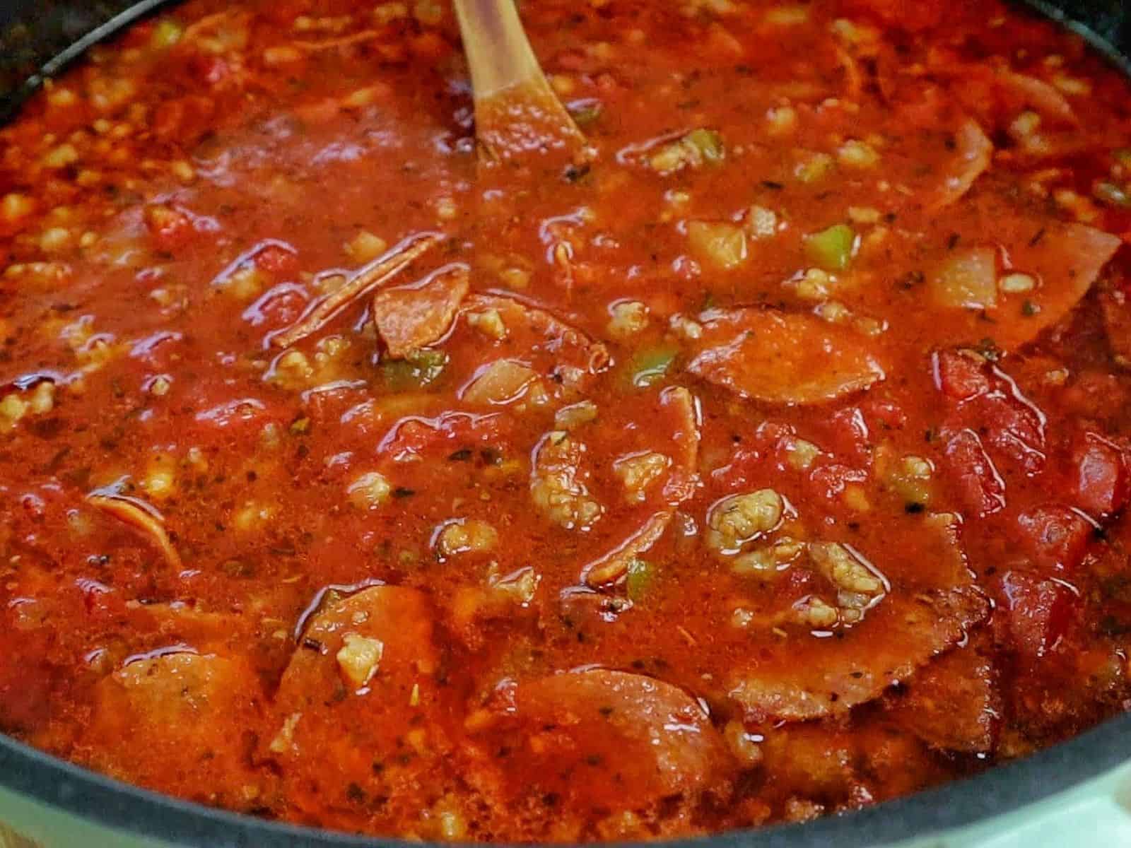 Homemade Meat Lovers Pizza Soup in a white bowl, loaded with Italian sausage, pepperoni, bacon, rich tomato broth, and shredded mozzarella and Parmesan cheese.
