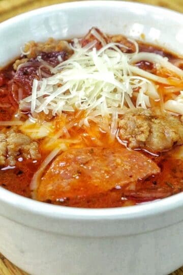 Homemade Meat Lovers Pizza Soup in a white bowl, loaded with Italian sausage, pepperoni, bacon, rich tomato broth, and shredded mozzarella and Parmesan cheese.