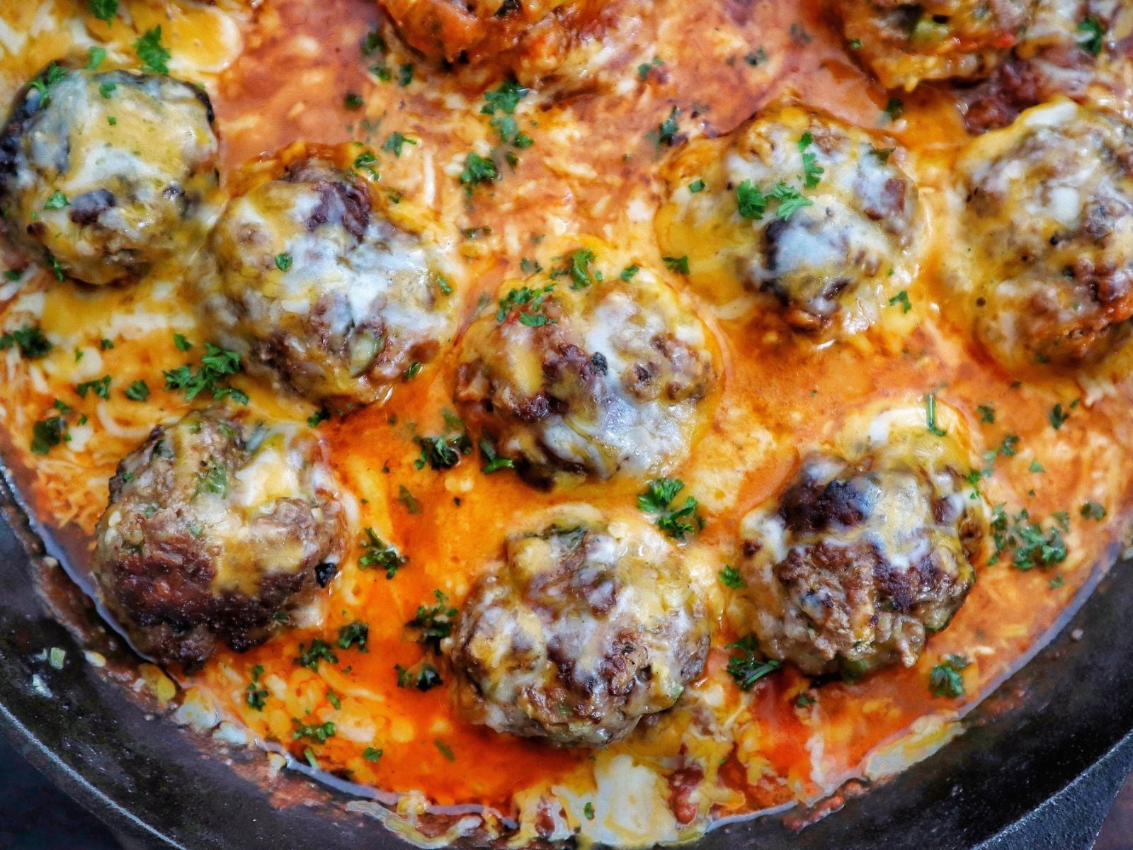 Juicy Tex-Mex meatballs topped with melted Mexican cheese in a smoky chipotle tomato sauce, garnished with fresh parsley in a cast-iron skillet.