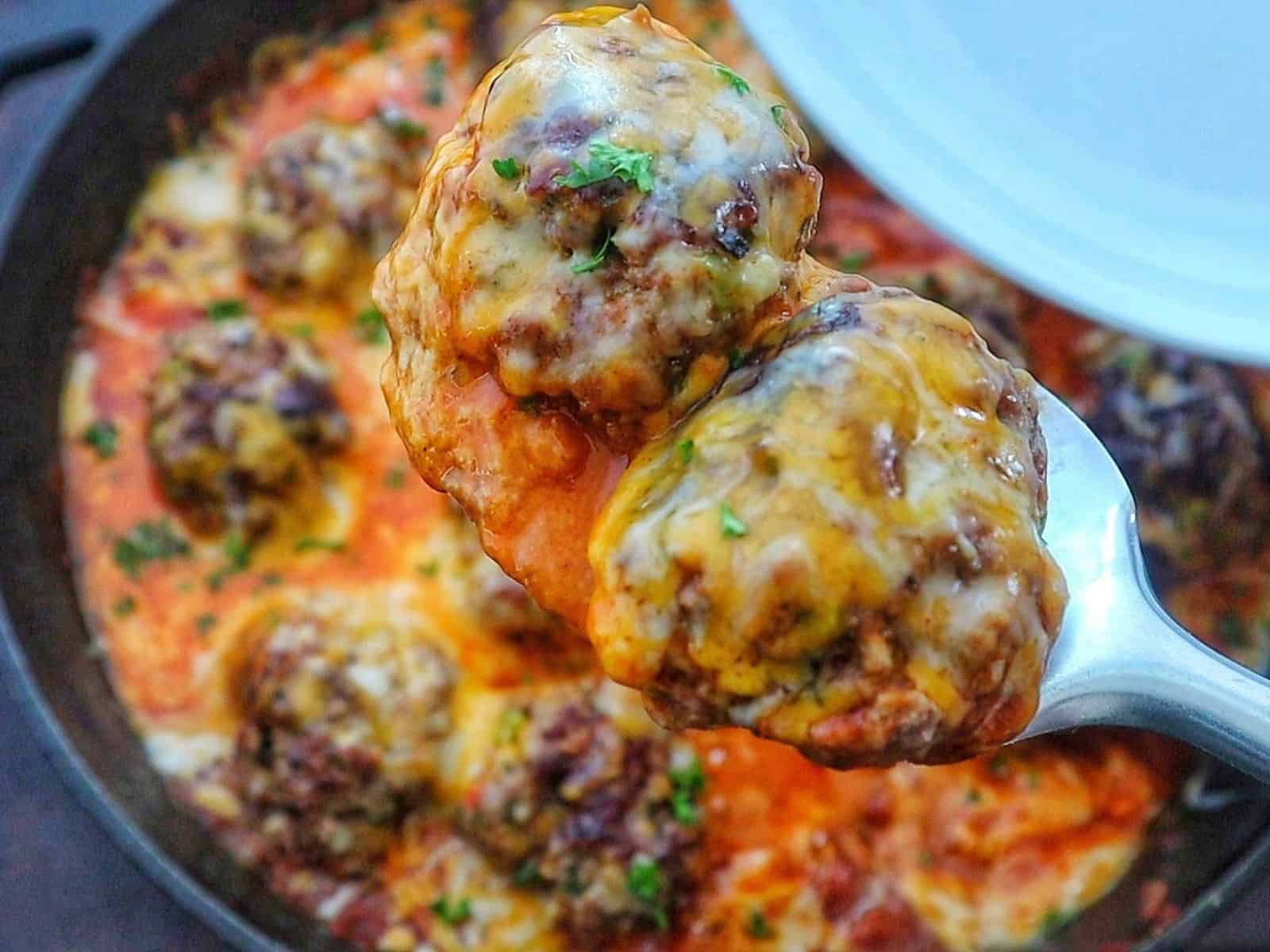 Juicy Tex-Mex meatballs topped with melted Mexican cheese in a smoky chipotle tomato sauce, garnished with fresh parsley in a cast-iron skillet.