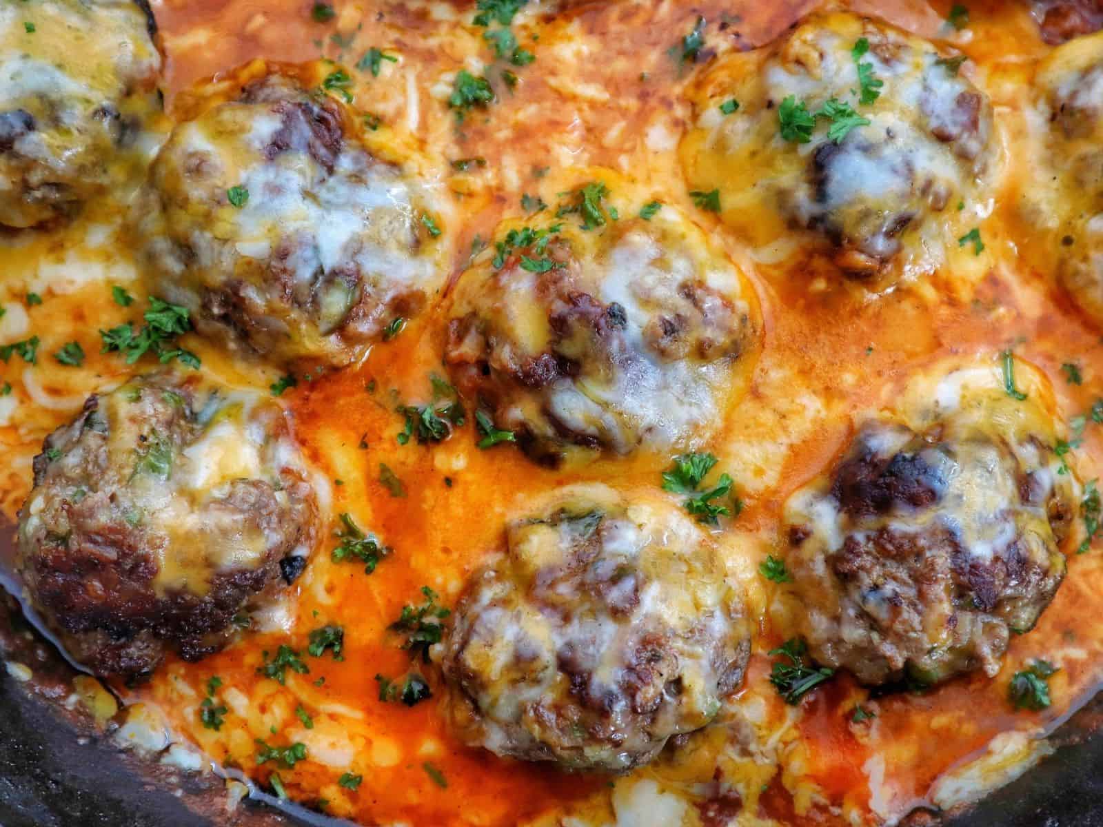 Juicy Tex-Mex meatballs topped with melted Mexican cheese in a smoky chipotle tomato sauce, garnished with fresh parsley in a cast-iron skillet.