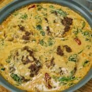 Pan-seared Tuscan Hamburger Steaks simmering in a rich Parmesan cream sauce with spinach, garlic and sun-dried tomatoes in a large skillet.