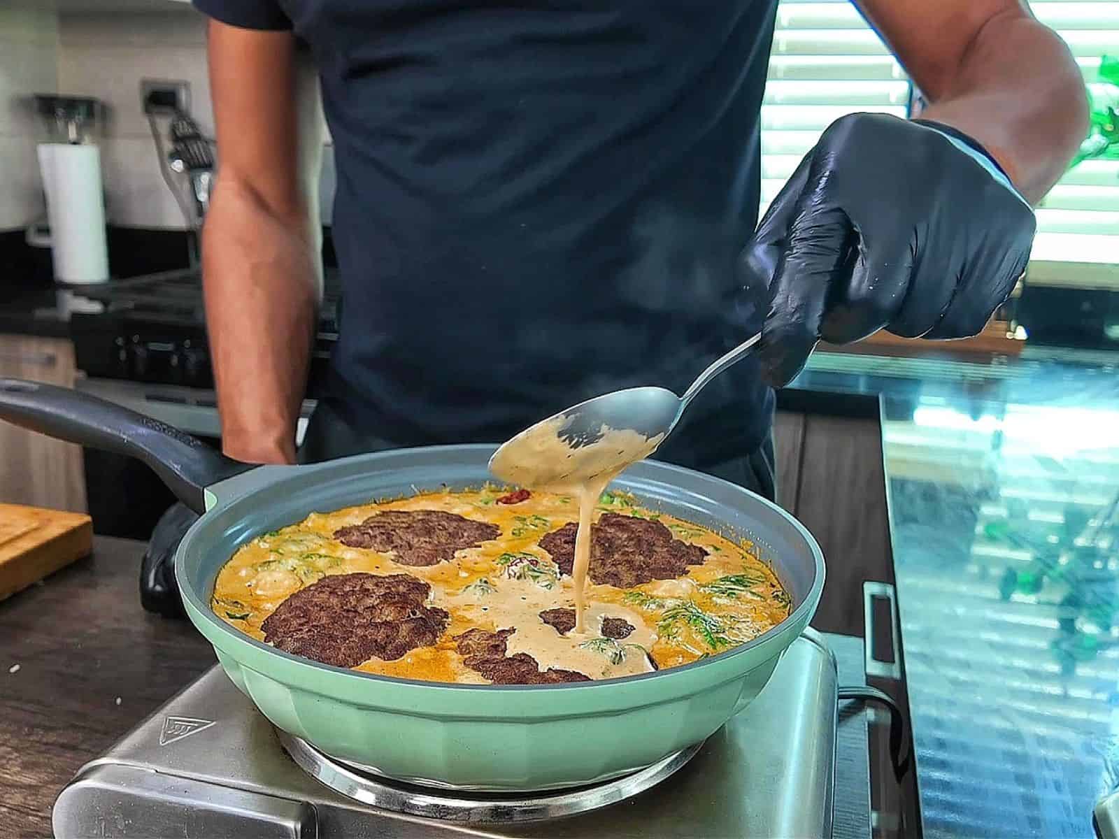 Pan-seared Tuscan Hamburger Steaks simmering in a rich Parmesan cream sauce with spinach, garlic and sun-dried tomatoes in a large skillet.