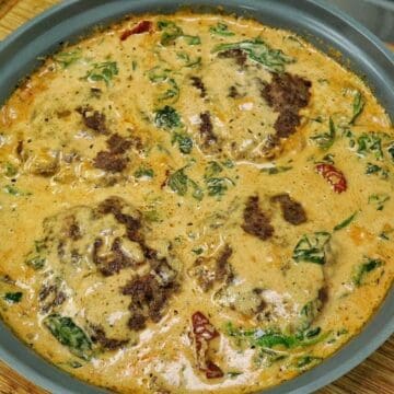 Pan-seared Tuscan Hamburger Steaks simmering in a rich Parmesan cream sauce with spinach, garlic and sun-dried tomatoes in a large skillet.