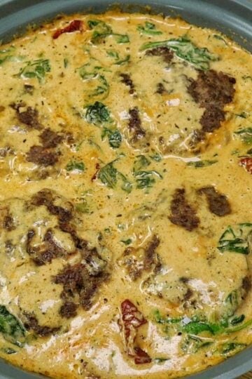 Pan-seared Tuscan Hamburger Steaks simmering in a rich Parmesan cream sauce with spinach, garlic and sun-dried tomatoes in a large skillet.
