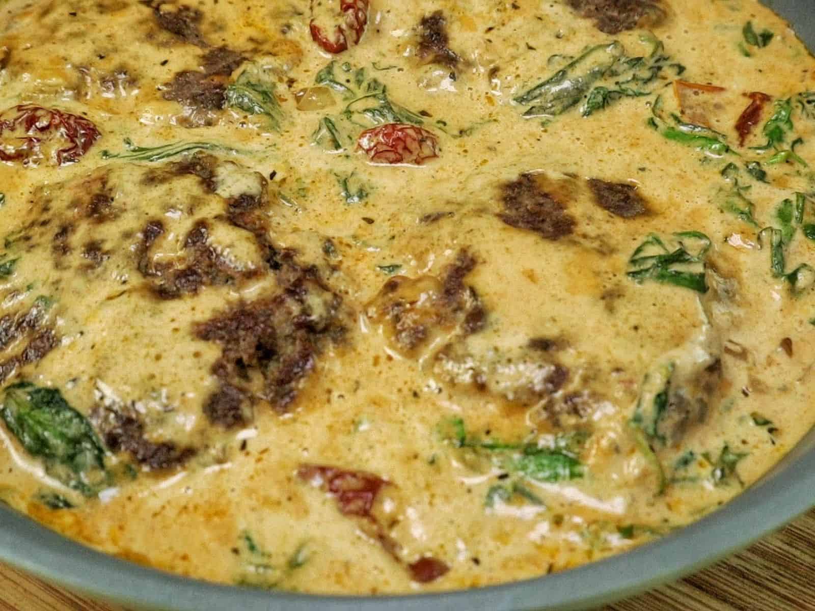 Pan-seared Tuscan Hamburger Steaks simmering in a rich Parmesan cream sauce with spinach, garlic and sun-dried tomatoes in a large skillet.